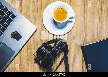 Wooden desk table with camera, laptop, memory cards, espresso cup and clipboard. View from top. Stock Photo