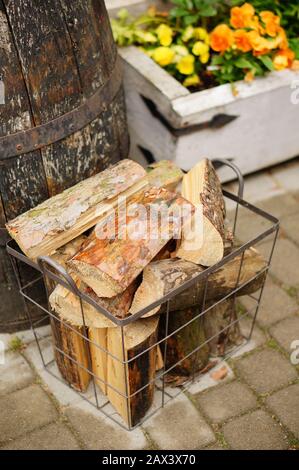 Basket of firewood on the ground in front of garden flowers and a wooden barrel Stock Photo
