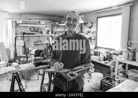 home Inspector taking notes during an inspection. A smiling caucasian aged man with glasses holds a notebook and pen, black and white Stock Photo