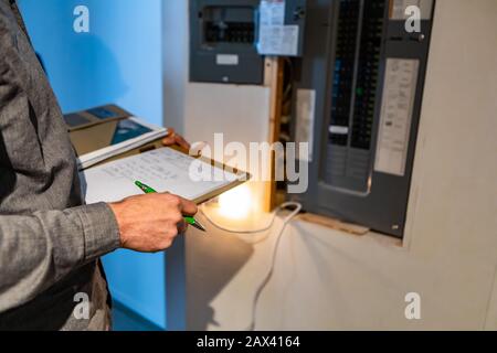 home Inspector in front of electric distribution board during inspection, selective focus and close up on man's hands as he holding notebook and pen Stock Photo