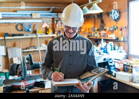 selective focus on Inspector in the garage interior during an inspection. middle aged caucasian man wearing helmet writes notes on a notebook Stock Photo