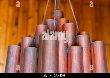 copper cylindrical tubes chandelier top in close up and selective focus view with a blurred wooden wall in the background Stock Photo