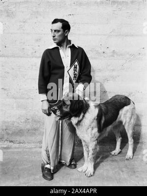 1930 ca , USA  : The american silent movie actor and director BUSTER KEATON ( 1895 - 1966 ) with his dog at Metro Goldwin Mayer lot Studios during the making of  a movie  - SILENT MOVIE - CINEMA MUTO  - portrait - ritratto -  regista cinematografico - attore  - comico   - COMICO -   ANNI TRENTA - 30's - '30 - trench - cane San Bernardo - sanbernardo - pet - animale domestico - scarpe - shoes - profilo - profile  ----  ARCHIVIO GBB Stock Photo