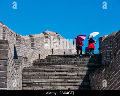 Chinese women holding sunshade parasols walking up steps at Jinshanling Great Wall of China in sunny weather, China, Asia Stock Photo