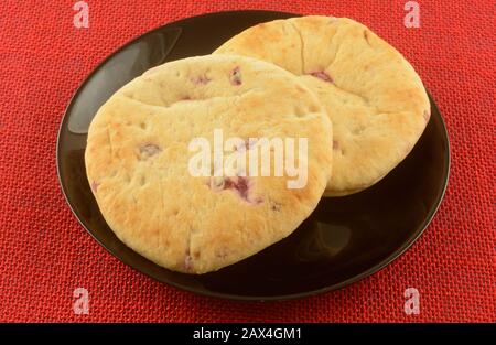 Two cranberry orange breakfast round loaves of breads on black bread on red tablecloth Stock Photo