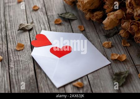Two red paper hearts, envelope and dry flowers on wooden table, toned vintage still life Stock Photo