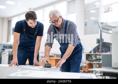 Serious senior specialist showing young worker how to stamp printed papers in printing house Stock Photo