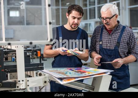 Busy printing plant workers standing at printed pages and choosing colors for next printing Stock Photo