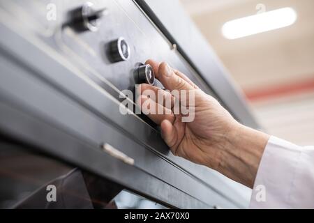 Close-up of unrecognizable man pushing button with arrow down while using automated factory machine Stock Photo