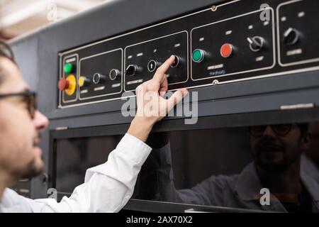 Over shoulder view of young operator pushing button on control panel while working in automated industry Stock Photo