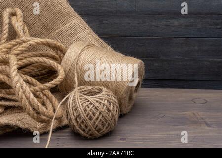 Two spools of burlap threads or jute twine and coil of linen rope on sackcloth fabric in close-up on grey background Stock Photo