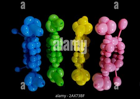 Colorful collection of pink, green, yellow, and blue inflated balloon poodle dogs with their reflection on a mirror against a black background. Stock Photo