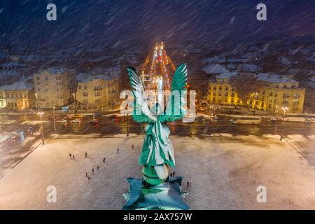 Budapest, Hungary - Aerial view of angel sculpture at Heroes' Square (Hosok tere) with Christmas decorated Andrassy street. Heavy snowing in Budapest Stock Photo