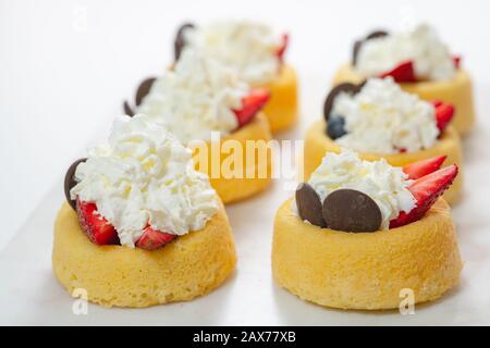 Biscuit cakes with fresh strawberries, blueberries, chocolate, and whipped heavy cream. Fresh mini biscuit cups close up on white background. Stock Photo