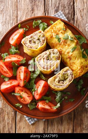 omelet roll stuffed with meat, cheese and pickles close-up in a plate on the table. Vertical top view from above Stock Photo