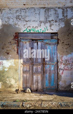 Closed wooden weathered door and shabby old grunge stone wall on abandoned district. Arabic text above door says: For Rent Stock Photo