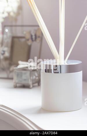Reed diffuser with sticks in a frosted glass jar on a white sideboard with ornaments Stock Photo
