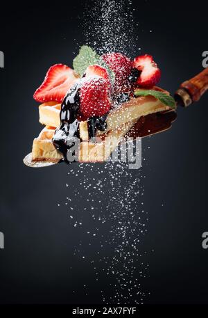 Belgian waffles with strawberries, mint and chocolate sauce, sprinkled with powdered sugar. Copy space. Stock Photo