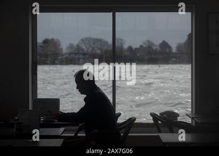 Bosham, West Sussex. 10th Feb 2020. UK Weather: A man is silhouetted in a cafe as tides rise in the wake of Storm Ciara and flood the village of Bosham, West Sussex, Uk Monday February 10, 2020.  Many places in the UK remain with yellow weather warnings as the Storm Ciara weather front continues.  Photograph : Luke MacGregor Credit: Luke MacGregor/Alamy Live News