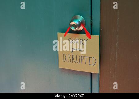 Closeup handwriting cardboard sign with message read sorry you are disrupted hanging on doorknob of wooden door, disruption concept Stock Photo