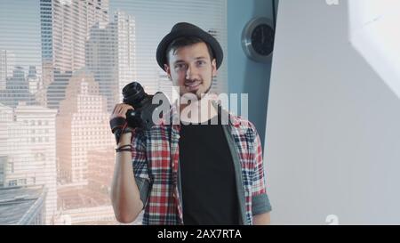 Portrait of young professional photographer in casual clothes with his camera smiling and posing. There are skyscrapers in the background. Stock Photo
