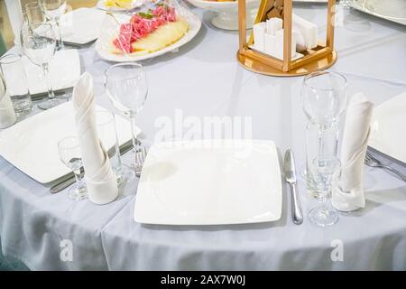 The table in the restaurant is served for dinner. On a table with a white tablecloth, empty wine glasses, a plates, napkins. Selective focus Stock Photo