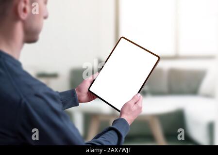 Man holding tablet with isolated screen in white for mockup. Living room interior in background Stock Photo