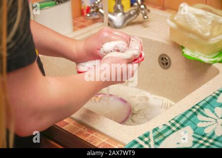 A woman washes dishes in the sink in her home kitchen Stock Photo