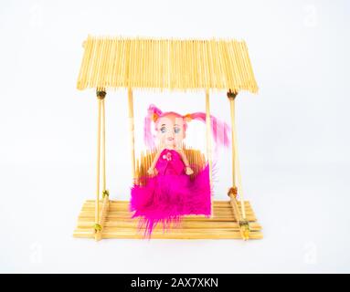 A handmade crafted doll in a pink dress on a miniature swing made of toothpicks Stock Photo