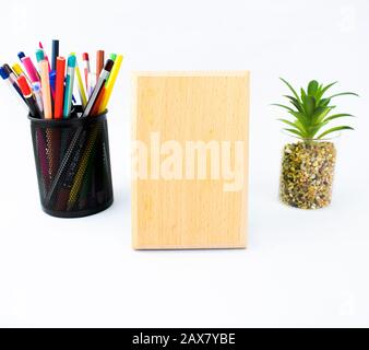 Wooden plaque which is with a black pencil holder full of crayons and a miniature tree on a white background Stock Photo