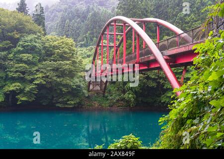 Turquoise blue water of forest lake with red arch bridge landscape. Japanese countryside view. Shima, Gunma prefecture, Japan Stock Photo