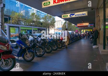 Melbourne, Australia - April 4, 2017: People walking street past scooters and motorcycles display Stock Photo