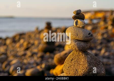 Balanced stone pyramide on shore of the ocean at dawn. Sea pebbles tower closeup symbolizing stability, zen, harmony, balance. Stock Photo