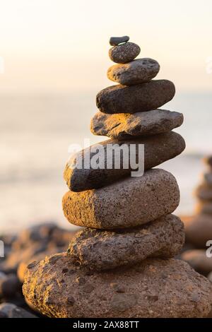 Balanced stone pyramide on shore of the ocean at dawn. Sea pebbles tower closeup symbolizing stability, zen, harmony, balance. Stock Photo