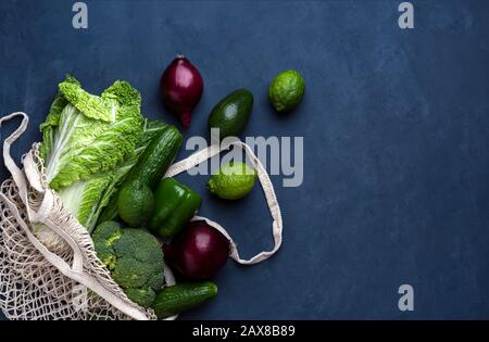 Fresh green and purple grocery bag items on a dark blue background. Top view with place for text. Stock Photo