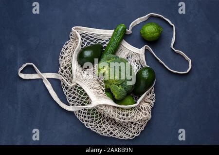 Reusable bag with green vegetables on a dark blue background. Mesh string bag, plastic free concept, top view Stock Photo