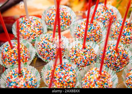 Delicious cake pops, sprinkled with colorful balls, lie on a glass stand. Stock Photo