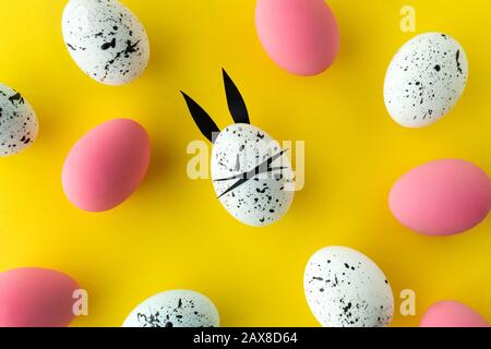Easter composition with colored eggs and egg with bunny ears and face on yellow background Stock Photo