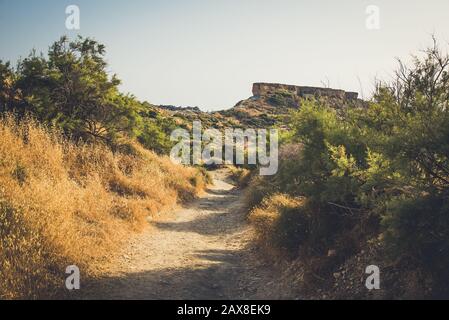 Dusty footpath under bright sun to the rock on the moountain Stock Photo