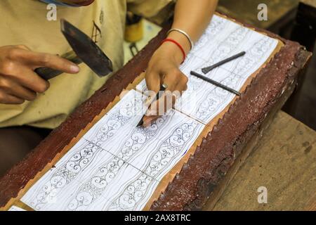 A woman using a hammer and chisel and a template to design a pattern on a piece of artwork at the workshops of Artisans d'Angkor, Siem Reap, Cambodia Stock Photo