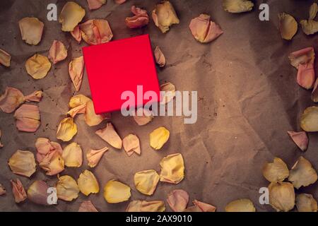 Red gift box with pink flower petals on crumpled kraft paper. Flat lay. Copy space on the box, for the brand. Suitable for layout. Vignetting. Stock Photo