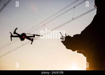 Man operating drone close to the electrical wire/ man holding remote control drones/drone controller. Stock Photo