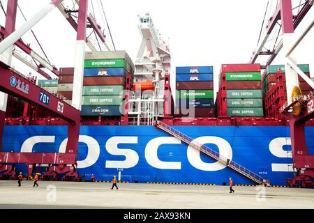 Port workers walk past a container ship docked on a quay at the Port of Qingdao in Qingdao City, east China's Shandong Province on February 11th, 2020 Stock Photo