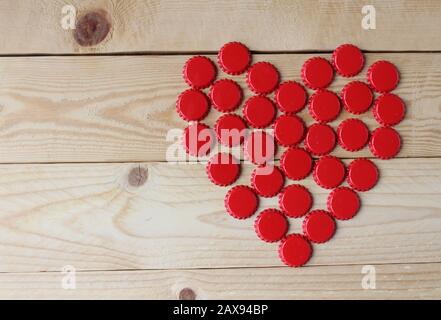 A red love heart made from beer bottle tops viewed top down on a rustic wooden table. Beer drinkers Valentine's day concept Stock Photo