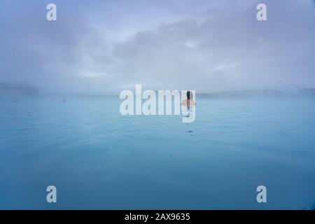 woman bathing in the Blue Lagoon next to Reykjavik with people bathing in this natural hot spring Stock Photo