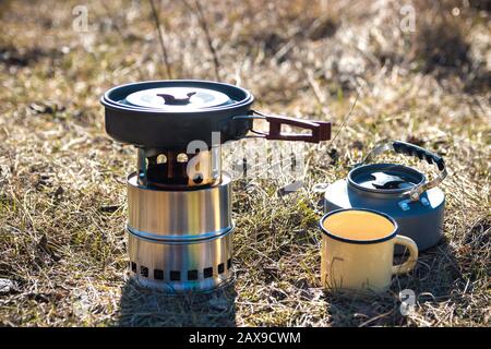 outdoor food preparation. closeup of frying pan portable wood stove, teapot and metal mug in mountains Stock Photo