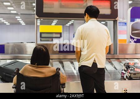 Caretaker with woman in wheelchair waiting for luggage on conveyor belt. Stock Photo