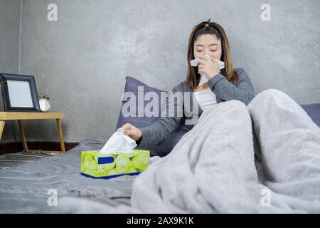 Sick day at home. Asian woman has runny nose and common cold. Cough. Beautiful Young Woman Caught Cold Or Flu Illness.