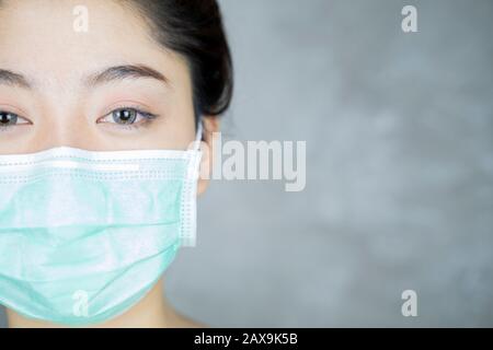 Close up portrait of young asian woman with medicine health care mask against grey room background. Stock Photo