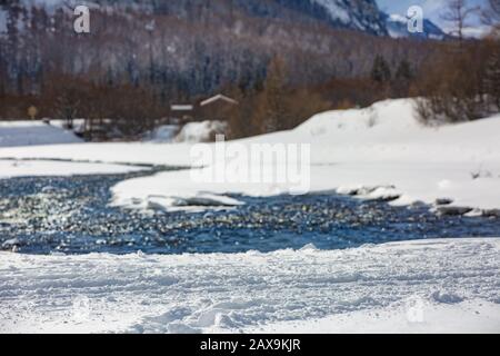 Snow trail in the foreground against the backdrop of a mountain river, alpine mountains and mountain hut. Selective focus, blur. France Stock Photo